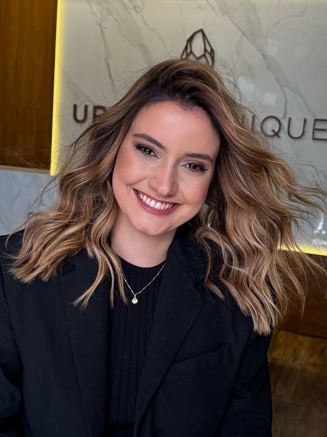 Cliente sorrindo na recepção, com o cristal da Urban Clinique na parede