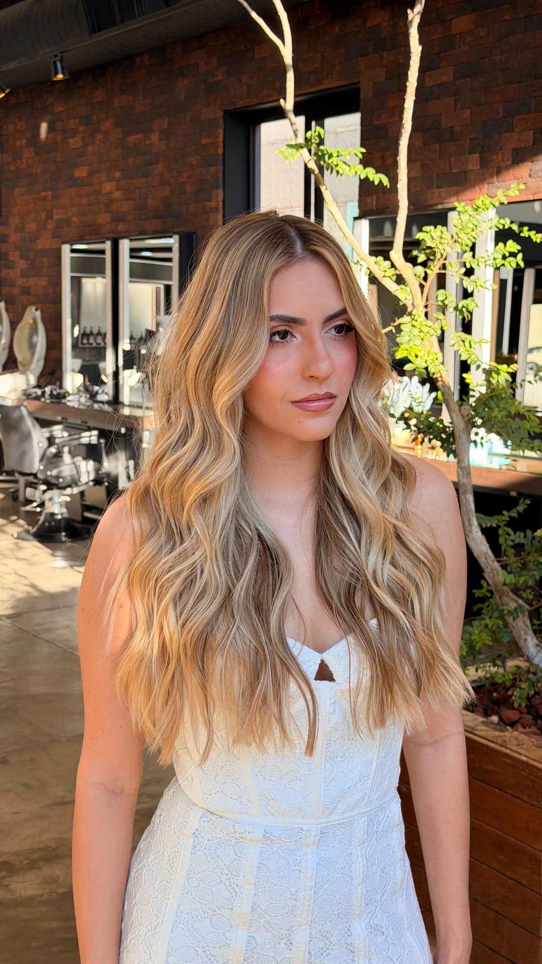 Cliente de loiro em ondas no salão, entre plantas e tijolo aparente